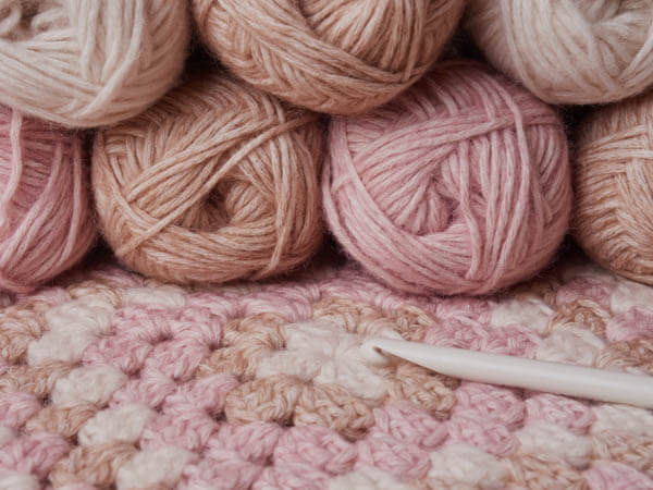 Pink and neutral ball of yarn, crochet hook and granny square